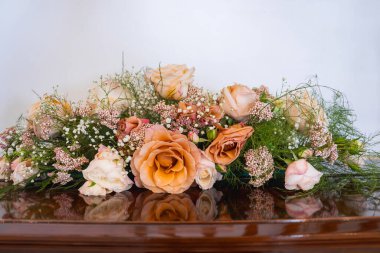 Şeftali ve allık güllerinden oluşan bir çiçek aranjmanı, bebek nefesi, ve parlak ahşap bir yüzeyde yeşillik, yumuşak pastel renkler ve zengin dokular sergiliyor..