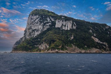 İtalya 'nın Capri şehrinde, turuncu ve pembe renkleriyle dolu, koyu mavi bir gökyüzünün altında, yeşil ve kayalık yüzeylerle çevrili dramatik bir uçurum..