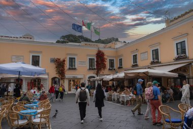 Capri, İtalya 'da hareketli bir meydan. Municipio binası, kırmızı tırmanma tesisleri, açık hava kafeleri, İtalyan bayrakları ve renkli bir günbatımı gökyüzü..