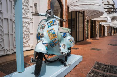 Capri temalı etiketleri olan klasik bir açık mavi Vespa, İtalya 'nın Capri şehrinde lüks mağazalar ve kemerli kapılarla döşenmiş tuğlalı bir sokakta sergileniyor..