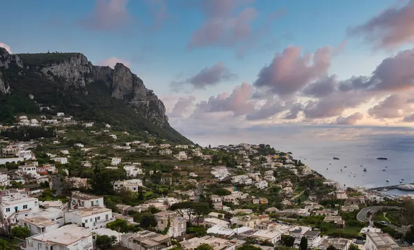 İtalya 'daki Capri adası beyaz boyalı binalar, kayalık bir uçurum, tekneli sakin bir deniz ve pembe ve mavi bir gökyüzü ile bir yamaçtır..
