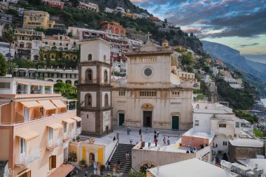 Positano, İtalya 'daki Santa Maria Kilisesi. Kubbesi ve çan kulesi, gün batımında teraslı binalar ve uçurumlarla çevrili..