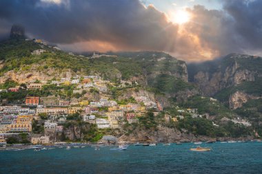 İtalya 'nın Amalfi Sahili' ndeki pozitano 'da dik bir yamaçta canlı binalar, tekneli turkuaz sular, engebeli uçurumlar ve dramatik gökyüzü yer alıyor..