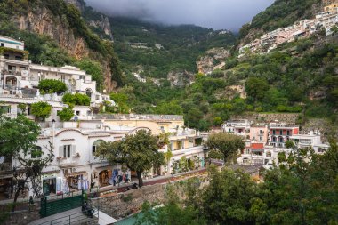 Positano, İtalya manzarası, yeşil bir yamaçtaki pastel renkli binalar, ağaç çizgili bir sokak, dik uçurumlar ve sisli bitki örtüsü..