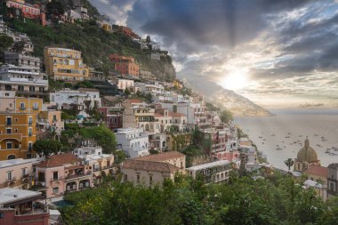 Dik bir yamaçtaki canlı binaları, Santa Maria Assunta Kilisesi 'nin kubbesi ve sakin mavi denizde kayıkları olan Positano, İtalya manzarası..