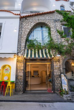 Otel Reginella 'nın taş cephesinde kemerli bir pencere, sarmaşık kaplı duvarlar, çizgili bir tente ve Positano, İtalya' da renkli tabureleri olan bir kafe bulunmaktadır..