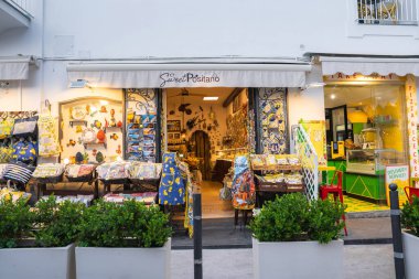 Positano, İtalya 'da renkli tekstil ve seramik ürünleri olan bir dükkan. Beyaz duvarlar ve yeşillikler çerçeveli sarı ve yeşil bir pizzacının yanında..