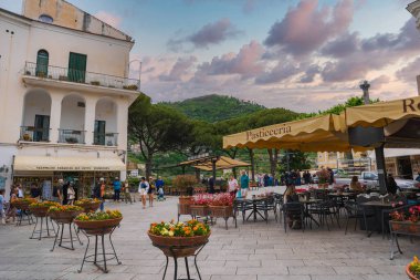 Ravello, İtalya 'da büyüleyici bir meydan. Sarı tenteli, canlı çiçekleri, hediyelik eşya dükkanı, yemyeşil tepeler ve bulutlu gökyüzü var..