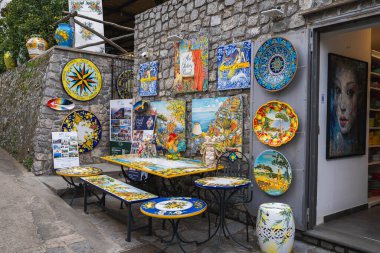 Ravello, İtalya 'da canlı bir seramik dükkanı. Renkli plakalar, fayanslar ve taş bir duvar zeminine karşı kıyı ve çiçeklerle süslenmiş masalar..