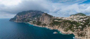 Capri Adası 'nın kıyı şeridi sarp kireçtaşı uçurumları, yeşil yamaçlarda beyaz yıkanmış binalar ve alçak asılı bulutların altında Tyrhenian Denizi' ne sahiptir..