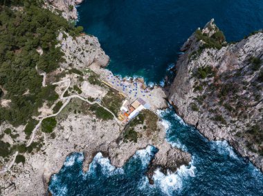 Capri Adası 'nın kayalık sahil manzarası, uçurumlar, turkuaz bir koy, şemsiyeli bir sahil, dolambaçlı yollar, ve Amalfi Sahili yakınlarındaki yemyeşil alanlar..