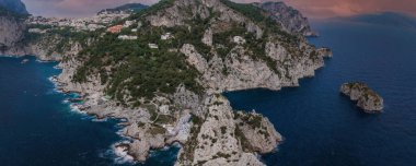 İtalya 'nın Capri Adası' nda yeşil ve beyaz villaları olan kireçtaşı uçurumlar, Tyrhenian Denizi ile çevrili ve pembe gökyüzü altında daha küçük kayalık çıkıntılar..