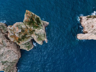 İtalya 'nın Capri Adası yakınlarındaki canlı mavi Akdeniz sularıyla çevrili yeşil ve turuncu bitki örtülü kayalık oluşumların hava manzarası.
