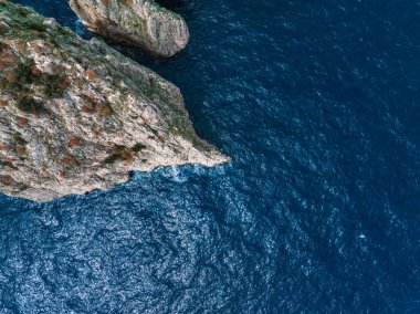 İtalya 'nın Capri Adası' ndaki mavi Akdeniz 'e uzanan yeşil ve turuncu bitkilerle kayalık uçurumların dramatik hava manzarası.