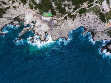 Capri Adası 'nın engebeli kayalıkları canlı mavi Akdeniz sularıyla karşılaşıyor. Patikaları ve seyrek yeşilliği olan küçük, gelişmiş bir bölge araziye karışıyor..