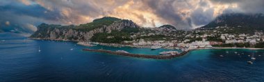 Capri Adası 'nın limanında yatlar, kıvrımlı dalgalar ve berrak sular bulunur. Beyazlaşmış binalar, dramatik kireçtaşı kayalıklarının altında yeşil tepelerde otururlar..