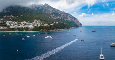 Capri Adası 'nın engebeli uçurumları, yeşillik içinde yüzen binalar ve Amalfi Sahili yakınlarındaki yatlar ve yelkenlilerle dolu canlı mavi sular..