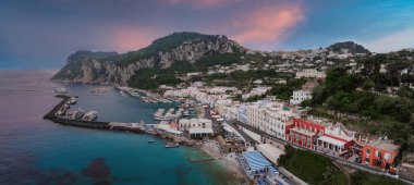 Capri Adası 'nın limanının manzarası. Tekneler, renkli rıhtım binaları, yeşil tepeler, kayalık uçurumlar ve gün batımında pembe ve mavi bir gökyüzü..