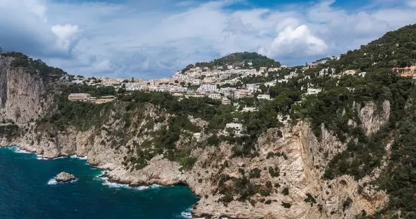 Yeşil sulara inen engebeli kireçtaşı kayalıkları yamaçtaki binalar ve parçalı bulutlu gökyüzünün altındaki kayalık çıkıntılar..