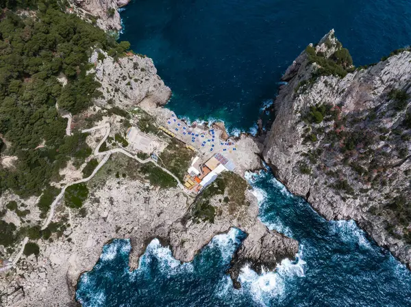 Capri Adası 'nın kayalık sahil manzarası, uçurumlar, turkuaz bir koy, şemsiyeli bir sahil, dolambaçlı yollar, ve Amalfi Sahili yakınlarındaki yemyeşil alanlar..