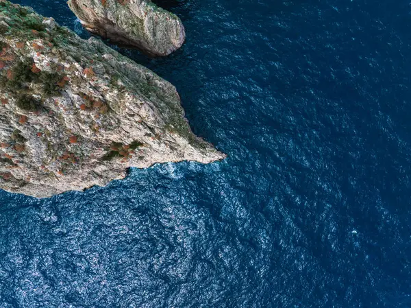 İtalya 'nın Capri Adası' ndaki mavi Akdeniz 'e uzanan yeşil ve turuncu bitkilerle kayalık uçurumların dramatik hava manzarası.