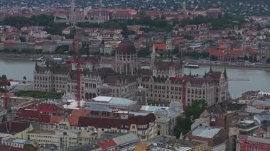 Macaristan 'ın Budapeşte kentinin havadan görünüşü, Macar Parlamentosu, Tuna Nehri, tekneler, çatılar, tarihi mimari ve inşaat vinçleri vurgulanıyor.