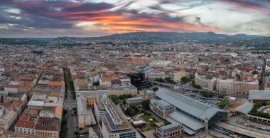 Budapeşte, Macaristan 'ın hava manzarası, Nyugati Tren İstasyonu, kırmızı kiremitli çatılar, Buda Tepeleri, ve canlı renklerle renkli günbatımı gökyüzü.