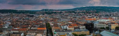 Budapeşte, Macaristan 'ın geniş hava manzarası, bir tepe üzerinde Buda Kalesi, Tuna Nehri, tarihi binalar ve bulutlu bir gökyüzünün altındaki uzak tepeler.
