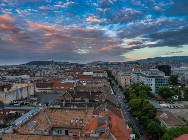 Macaristan 'ın Budapeşte kentinin havadan görünüşü, kırmızı kiremitli çatılar, ağaç kaplı caddeler, uzak tepeler ve gün doğumunda veya günbatımında renkli bir gökyüzü.