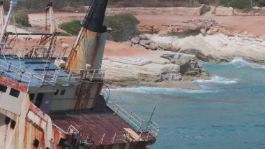 Kıbrıs 'ta kayalık bir kıyı şeridi yakınlarındaki turkuaz sulardaki Edro III Gemi enkazının hava manzarası. Kibar dalgalar ve sahil boyunca yürüyen ziyaretçiler görülebilir..