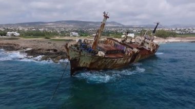 Kıbrıs 'taki Edro III enkazının etrafındaki hava tavası, paslı yapısını, kayalık kıyı şeridini, mavi sularını ve bulutlu gökyüzünün altındaki uzak tepeleri gösteriyor..