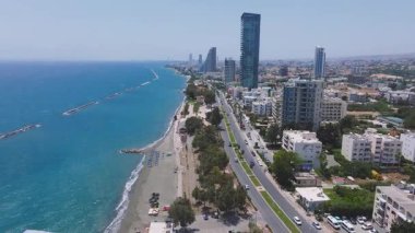 Kıbrıs Rum Kesimi 'nin Limasol kentinin havadan görünüşü, kumlu bir sahil, dalga kırıcılar, modern yüksek binalar, trafiğin olduğu bir ana yol ve Akdeniz' i gösteriyor..