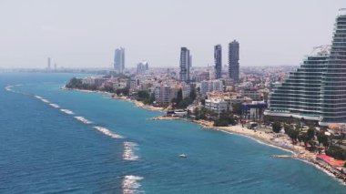 Kıbrıs 'ın Limasol kentsel binaları, gezinti güvertesi, sahil ve turkuaz Akdeniz suları basamaklı bir gökdeleni gösteriyor.