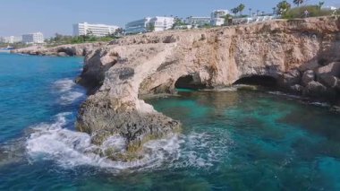 Kıbrıs Rum Kesimi 'nin Ayia Napa kentinin hava manzarasında Aşk Kemeri, turkuaz sular, modern tatil beldeleri, yemyeşil otlar ve kıyı boyunca hafif dalgalar yer alıyor..