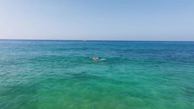 Kıbrıs 'ın Ayia Napa kenti yakınlarındaki kristal berrak turkuaz sularda sırtüstü yüzen bir adam nazikçe hareket ediyor ve sualtı arazisini ortaya çıkaran dalgalar yaratıyor..