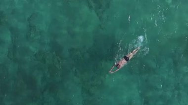 Kıbrıs Rum Kesimi 'nin Ayia Napa kenti yakınlarındaki berrak turkuaz sularda yüzen bir yüzücünün sakin hava görüntüsü, sakin denizde dalgalanmalar ve sıçramalar görülüyor..