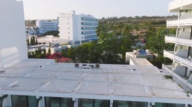 Kıbrıs Rum Kesimi 'nin Ayia Napa kentindeki bir tatil beldesinde pürüzsüz bir insansız hava aracı uçuşu, beyaz binalar, dolambaçlı bir havuz, yemyeşil ve canlı çiçekleri gösteriyor..