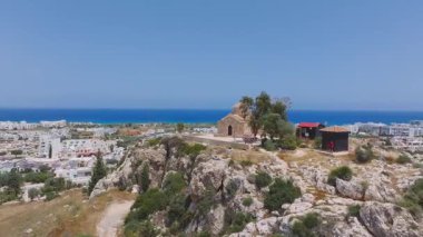 Pürüzsüz insansız hava aracı uçuşu Kıbrıs 'ın Ayia Napa kentindeki kayalık bir tepede uçurumlar, yeşillikler ve aşağıda genişleyen bir kasaba manzarası olduğunu ortaya çıkardı..