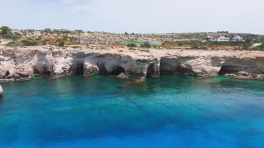 Kıbrıs Rum Kesimi 'nin Ayia Napa kentindeki kayalık bir kıyı bölgesinin hava temizliği, aşk heykelinin yer aldığı seyrek trafikli bir yol ve arka planda dağınık binalar.