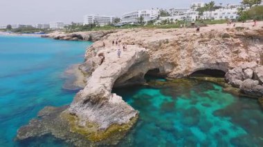 Ayia Napa 'nın turkuvaz suları, uçurumlardaki insanlar ve denize atlayan bireylerin hareketleri ile Aşk Kemeri oluşumu. Görünür engebeli arazi.
