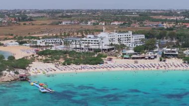 Kıbrıs Rum Kesimi 'nin Ayia Napa kentinin havalimanı turkuaz suları, sahil beldesi, güneşlik yatakları, yemyeşil alanlar ve kasabanın kentsel ve kırsal manzarasını gösteriyor..