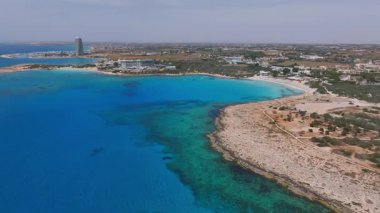 Kıbrıs Rum Kesimi 'nin Ayia Napa havalimanı turkuaz suları, canlı plajlar, sahil beldeleri, modern bir kule ve yemyeşil alanları gösteriyor..