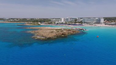 Kıbrıs Rum Kesimi 'nin Ayia Napa kentinin hava manzarası, Nissi sahilini mavi şemsiyeli, turkuaz sulu, modern tatil beldeleri, palmiye ağaçları ve yemyeşil yemyeşil.