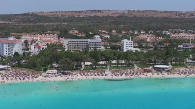 Kıbrıs Rum Kesimi 'nin Ayia Napa havalimanı, turkuaz suları, kumlu plajları, palmiye ağaçları, güneşli banyoları ve uzak arazisi olan beyaz bir oteli gösteriyor..