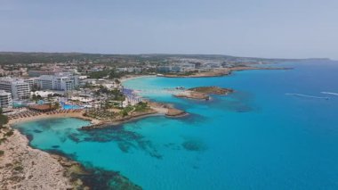 Ayia Napa 'nın sahil şeridinde hava temizliği, Nissi Sahili, turkuaz sular, tatil evleri, havuzlar ve yemyeşil alanlar.
