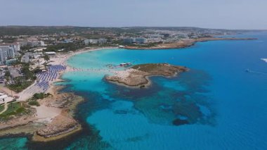Kıbrıs Rum Kesimi 'nin Ayia Napa kentinin geniş çaplı hava manzarası, turkuaz sular, kumlu Nissi plajları, kayalık kayalıklar, tatil beldeleri ve kıyı şeridi boyunca uzanan sahil ziyaretçileri.