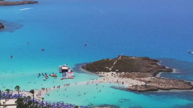 Ayia Napa 'nın turkuvaz suları, Nissi Sahili, güneşlik yatakları, şemsiyeler, modern tatil beldeleri ve hareketli yemyeşil alanları ile kıyı şeridinin havadan görüntüsü..