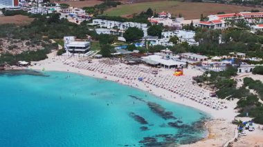 Kıbrıs Rum Kesimi 'nin Ayia Napa kentinin havadan görünüşü turkuaz suları, kumlu plajları, kıyıya yakın tekneleri, tatil merkezlerini ve çevresindeki yeşillikleri gösteriyor..