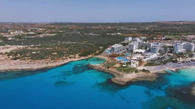 Kıbrıs 'ın Ayia Napa kentinin hava manzarası, Nissi Sahili, turkuaz sular, kumlu plajlar, kayalık çıkıntılar ve hareketli yakın tatil beldeleri.