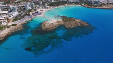 Kıbrıs Rum Kesimi 'nin Ayia Napa kentinin havadan görünüşü, beyaz kum, turkuaz sular, modern tatil beldeleri ve kıyı şeridi üzerindeki hareketli Nissi Sahili.